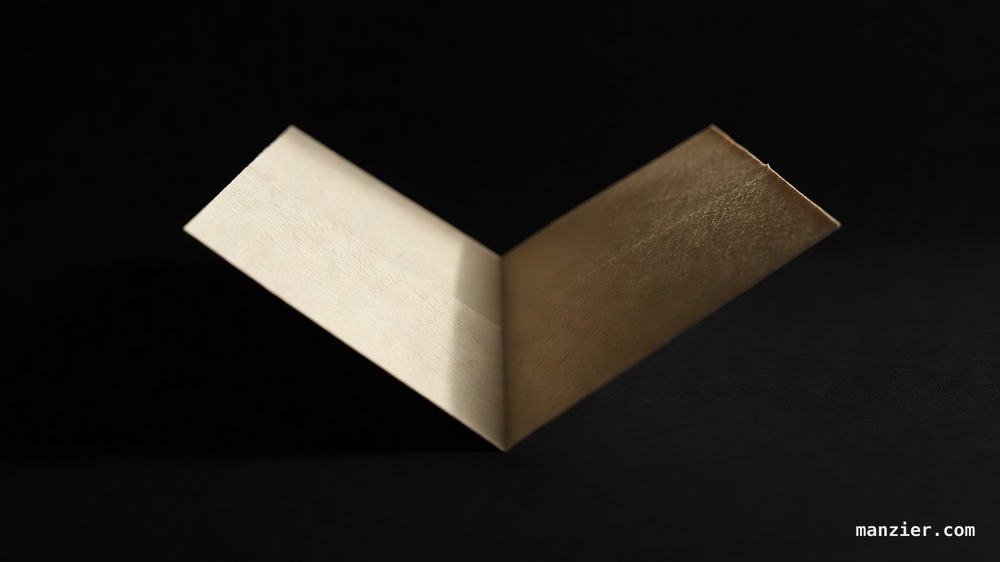 Extreme macro of a single sheet of cream paper folded into a sharp valley fold under raking amber light against black